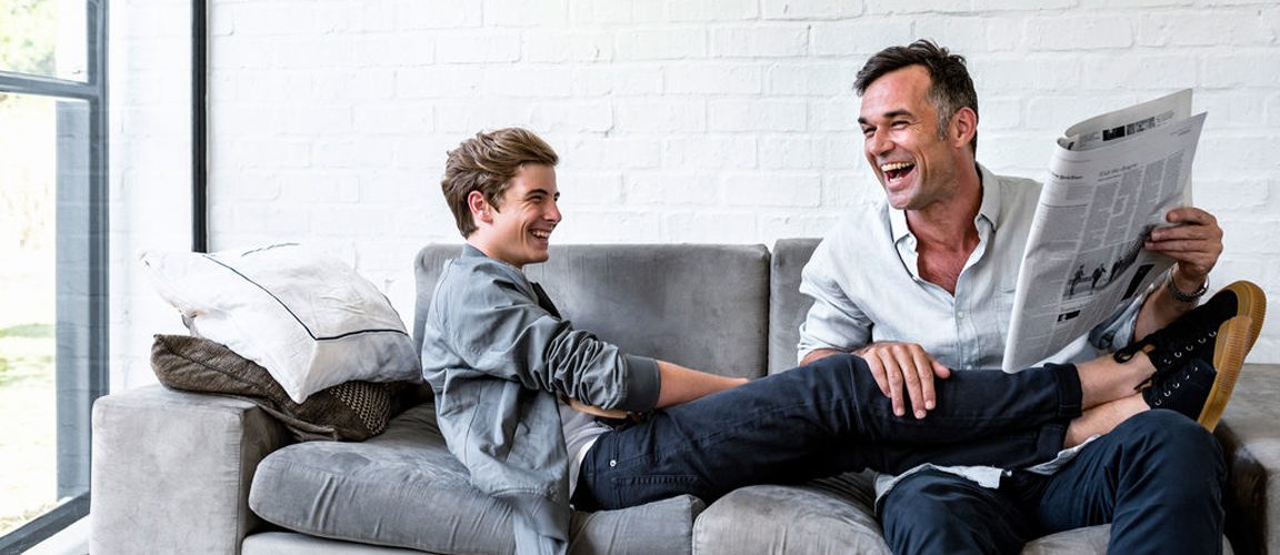 Father and teenage son sitting on couch laughing